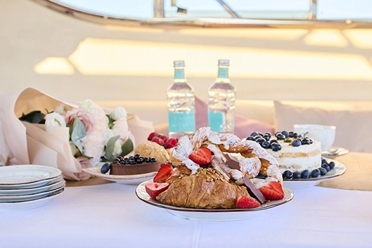 Tiered birthday cake surrounded by colorful party snacks on buffet table